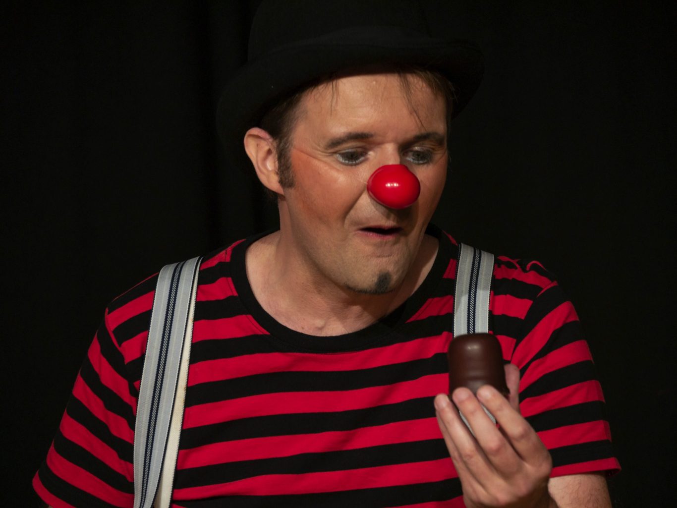 Clown in gestreifter Kleidung und roter Nase hält einen Schokokuss in der Hand.